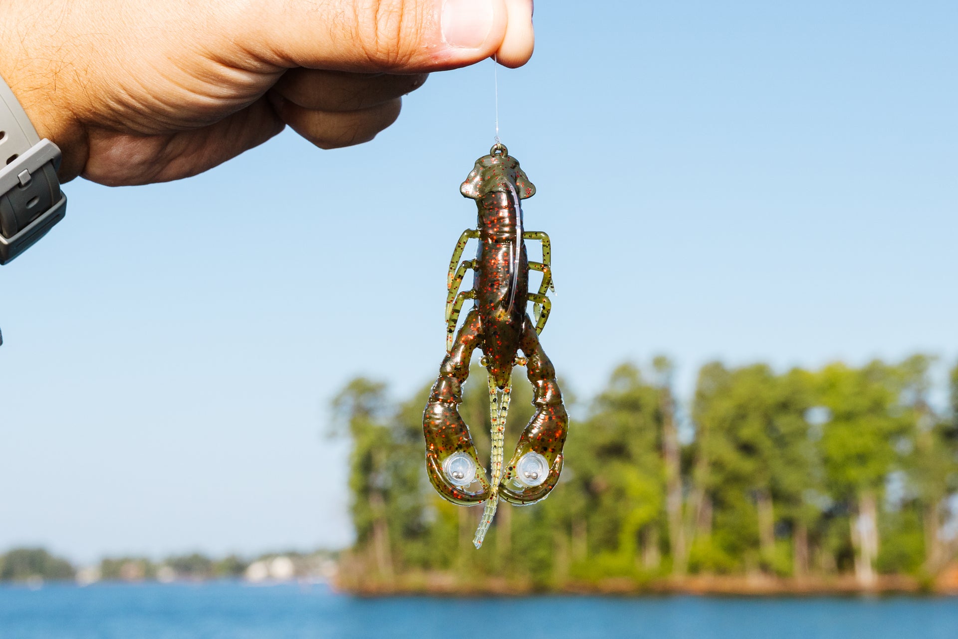 Man holding a Berkley PowerBait® Clatter Craw bait hanging from a fishing line above the water